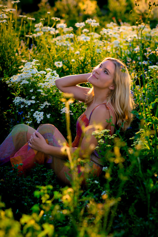 Blonde girl looking up while sitting in a field of flowers for senior pictures 