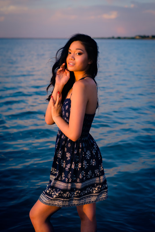 Girl in blue dress standing in ocean or lake with golden sun for senior pictures