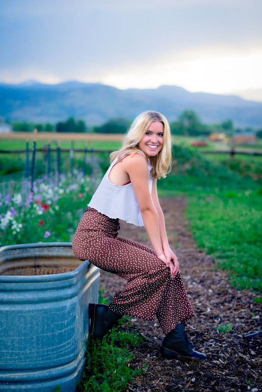 Girl sitting on a water grate leaning onto her knees smiling at camera for senior pictures 