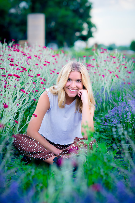 Girl sitting in a purple flower field wearing a white shirt brown polka dot pants for senior pictures