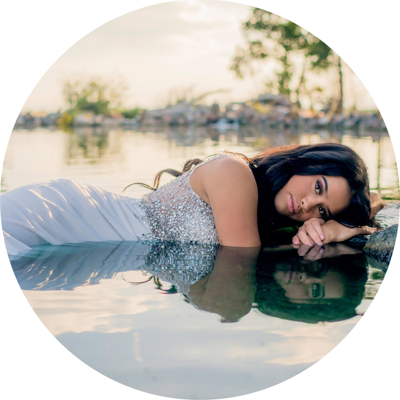 senior picture of girl with dark hair laying in pool of water in white prom dress in Denver Colorado