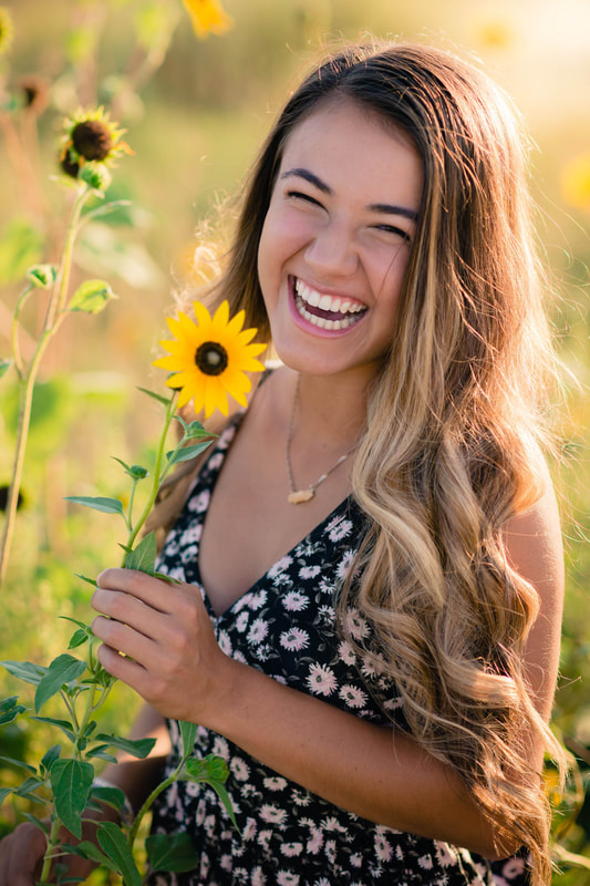 Girl holding sunflower laughing for senior pictures in Denver Colorado