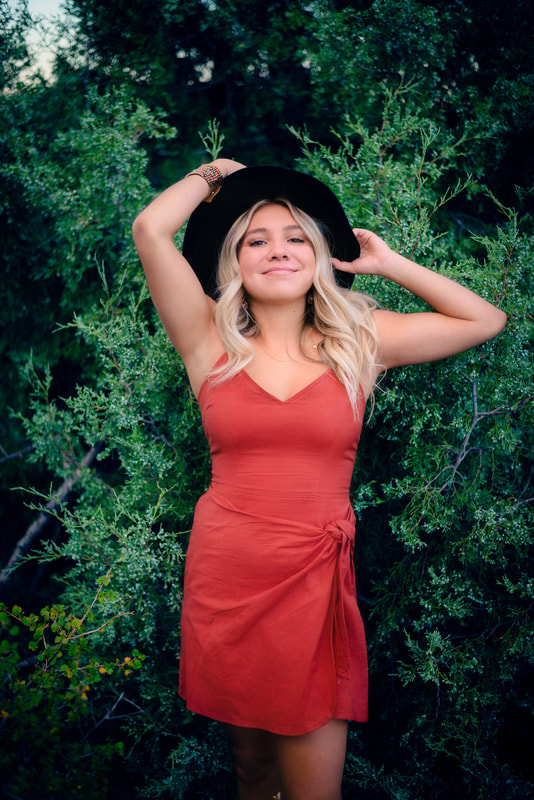 Girl wearing rust colored dress and a hat for senior pictures 
