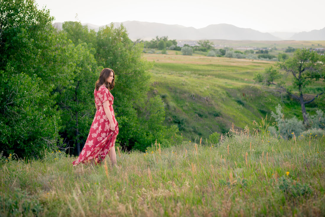 Girl in red dress walking through lush green field for senior pictures 