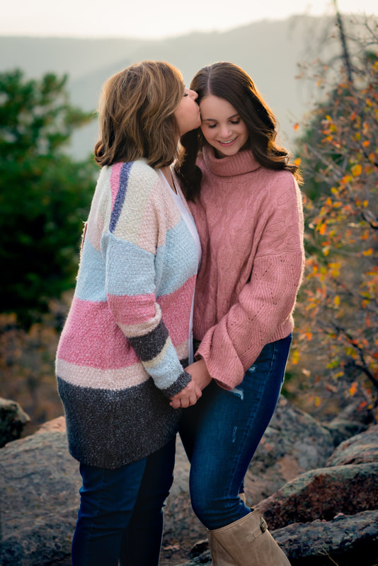 Mother kissing daughters forehead with a colorful fall background for senior pictures