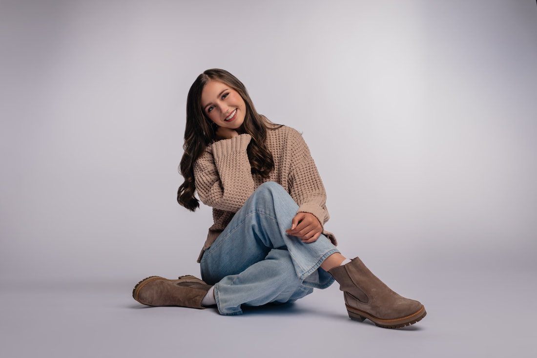 Girl sitting in a studio space brown knit sweater and blue jeans for senior photoshoot Parker Colorado