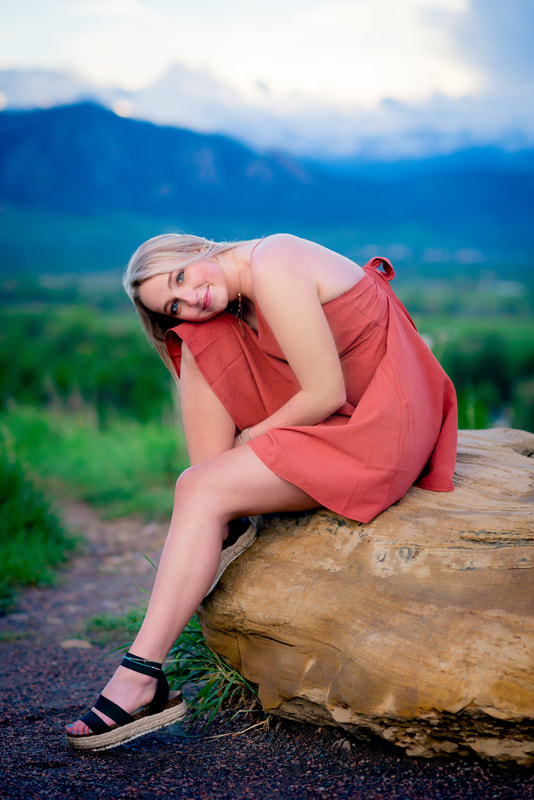 Girl in red dress sitting on rock for senior pictures 