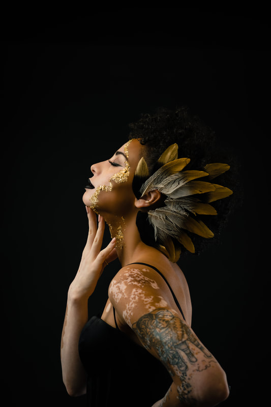 Girl vitiligo with Feathers in her hair, gold decorations on her face dark studio background Denver Colorado Senior Photoshoot