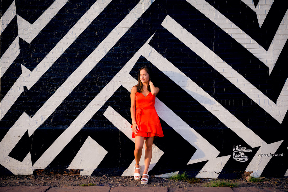 Girl in red dress standing against a black and white wall for senior pictures 