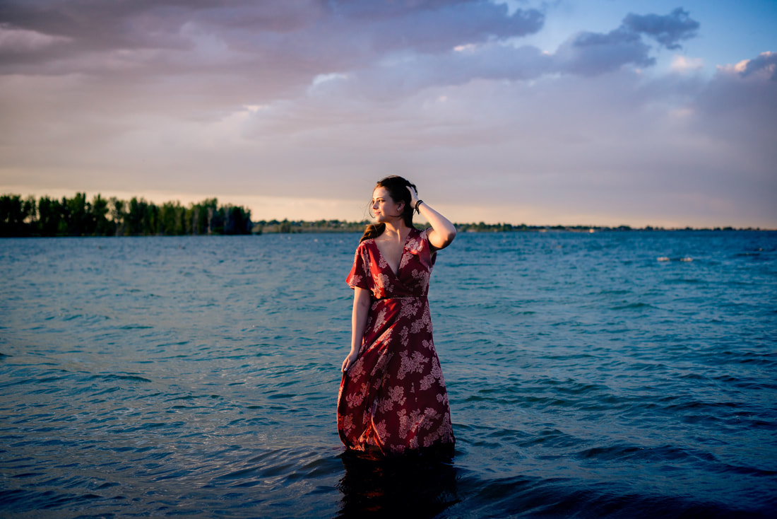 Girl standing in a lake at sunset playing with her hair for a fun senior picture shot