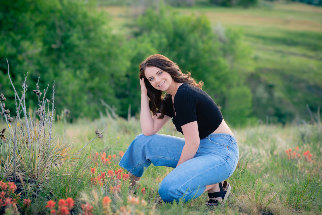 Girl kneeling down playing with her hair in a field for senior pictures