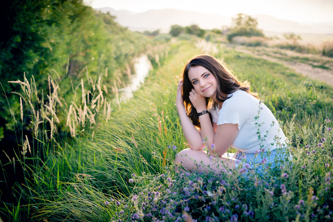 Girl in white shirt and blue shorts sitting along a creek for senior pictures