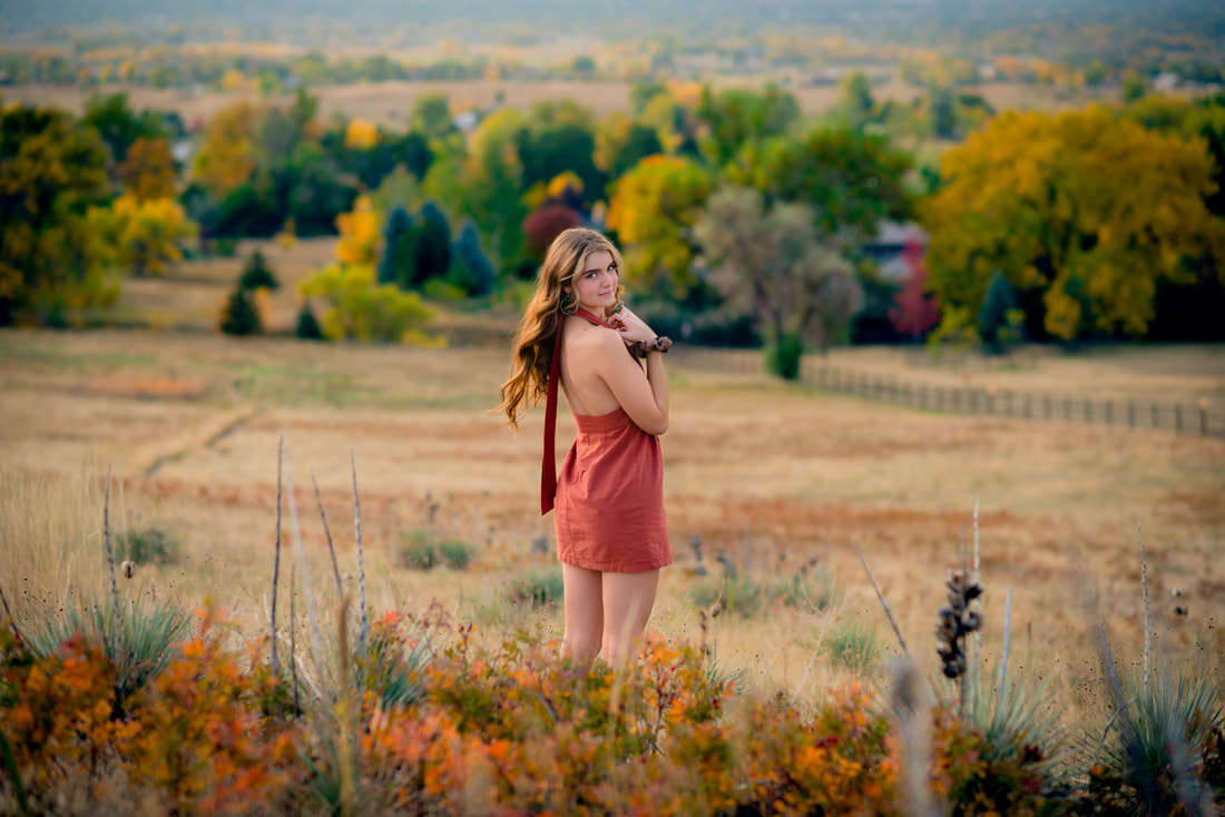 Girl in rust dress looking back at camera with fall colors surrounding her for senior pictures 