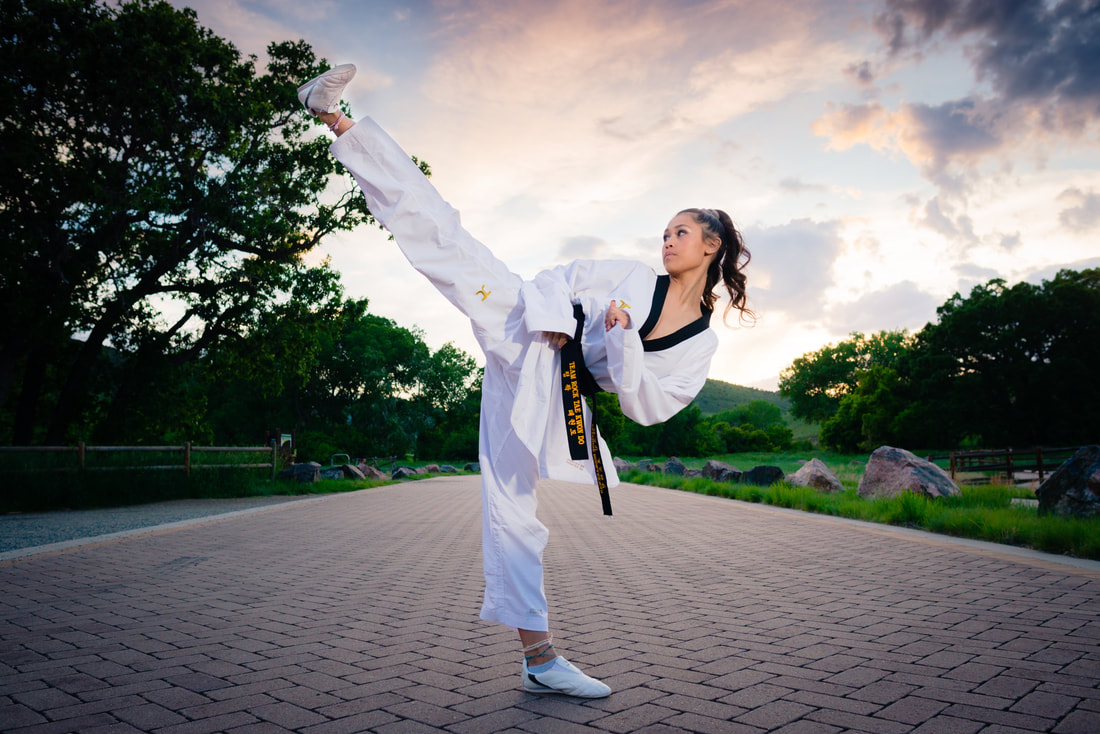 girl in karate uniform kicking in front of sunset for senior pictures