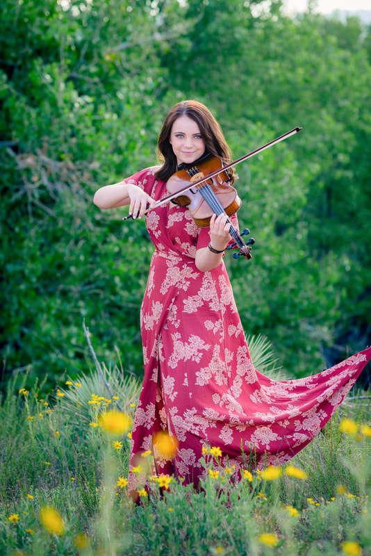 Girl in red dress standing in a field of flowers playing the violin for senior pictures