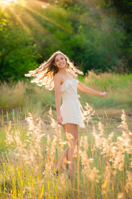 A portrait of a young woman with a light-colored outfit smiling and twirling towards the camera.