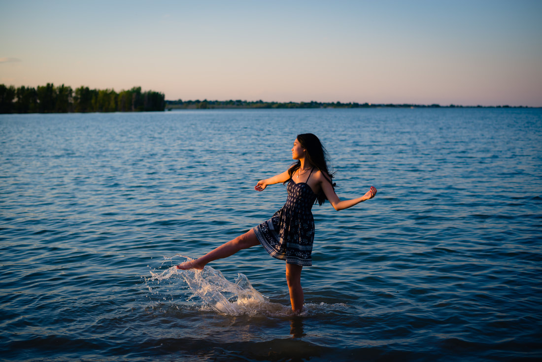 Girl in sundress kicking the water creating a splash for senior pictures