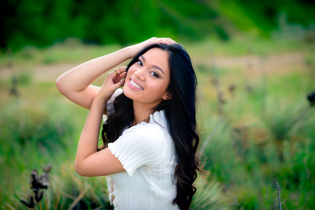 girl in green field smiling at camera for senior pictures 