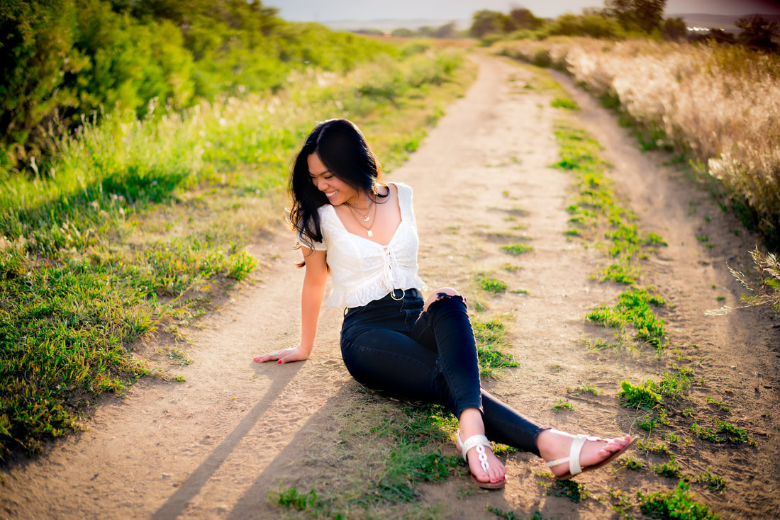 Girl sitting on a path looking away from the camera smiling for senior pictures 