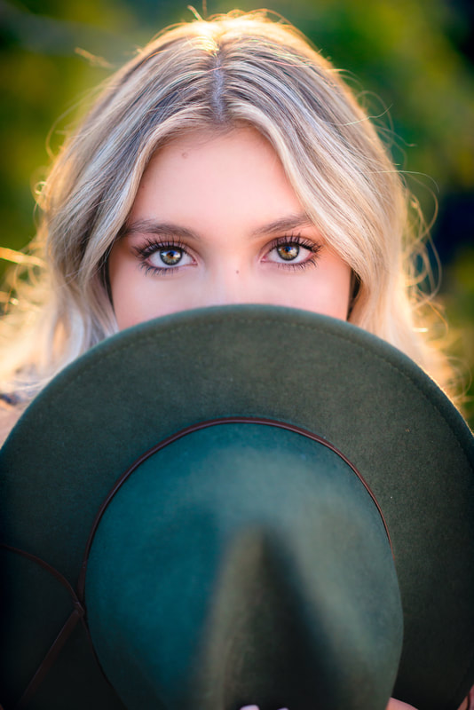 Girl with brown eyes holding a hat over her nose and mouth for senior pictures