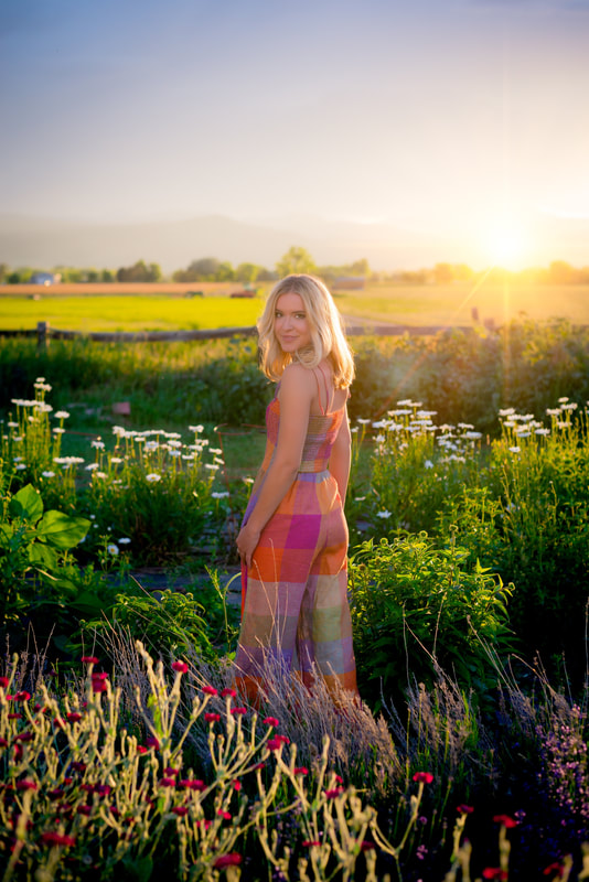Girl in rainbow colorful romper jumpsuit in field of flowers with golden sunset for senior pictures