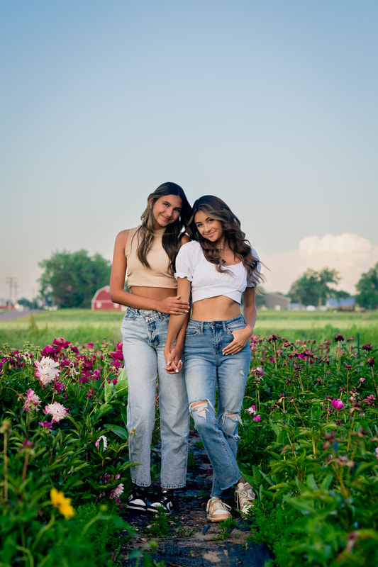 Two girls in a flower field wearing blue jeans and tank tops for senior pictures parker colorado