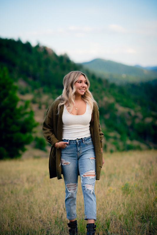 Girl walking in mountain meadow with blue jeans and green sweater for perfect senior pictures