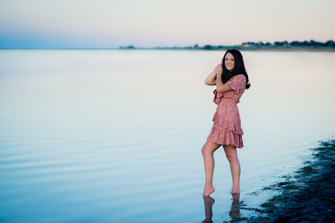 Brunette girl in pink dress standing in water for senior pictures