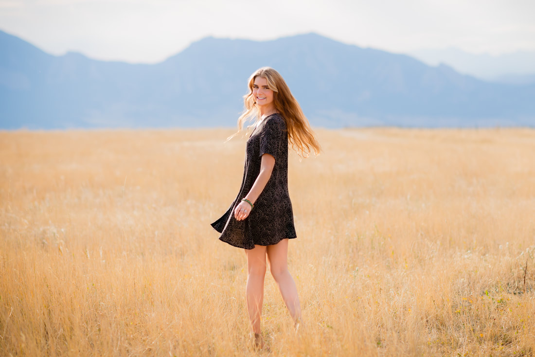 Girl in black dress standing in a straw field for senior pictures 