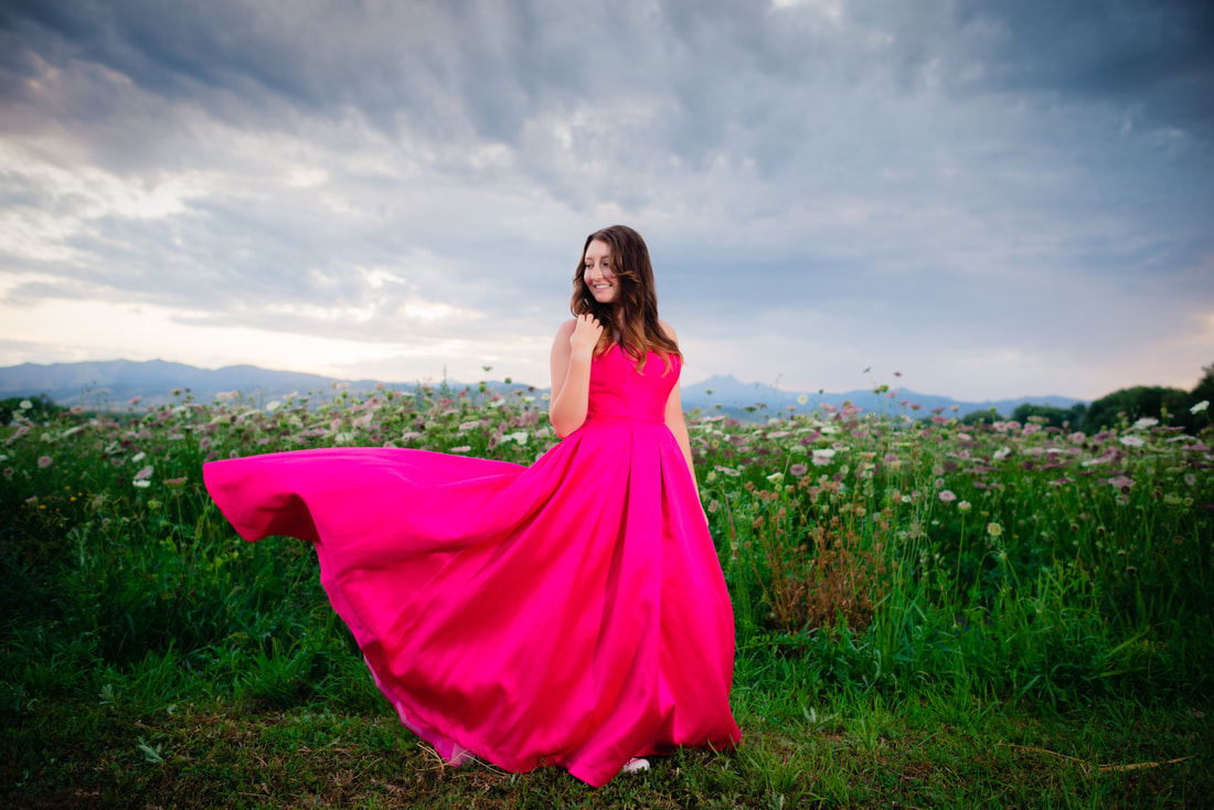 girl in bright pink dress looking over her shoulder and a stormy sky behind her for senior pictures