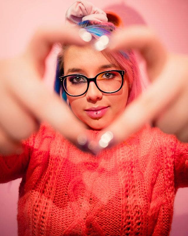 Girl in pink sweater holding fingers in heart shape with glasses for senior pictures