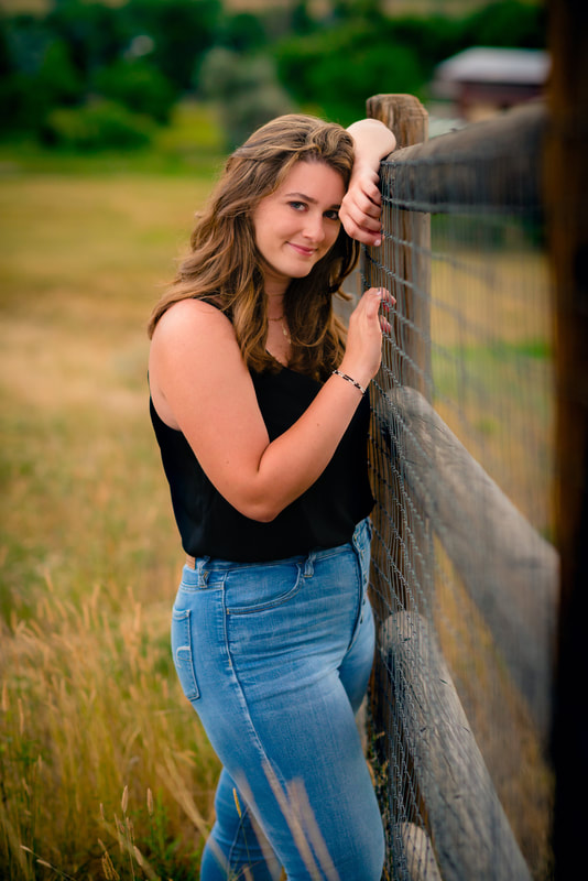 Brunette girl leaning on a fence looking at camera for senior pictures 