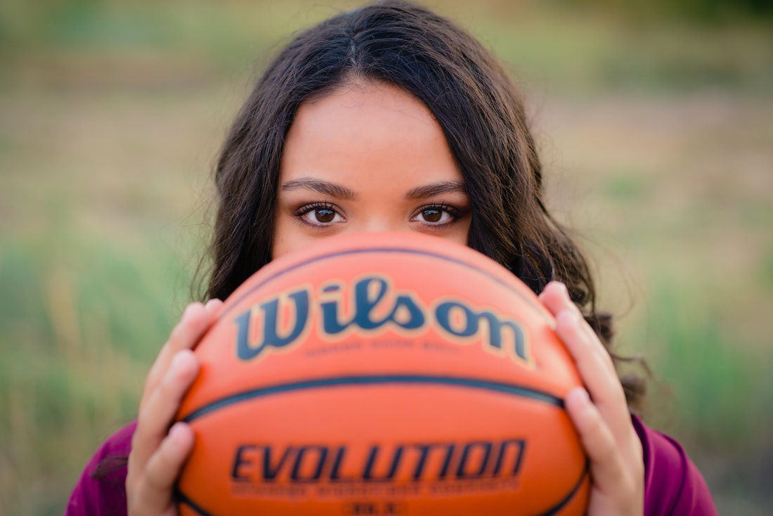 Girl holding basketball in front of face for senior pictures