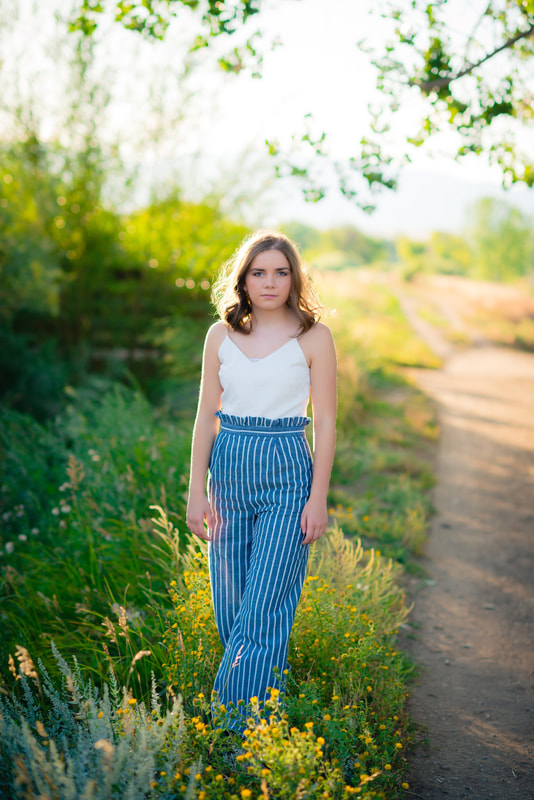 Girl in white shirt and pinstripe blue pants standing in sunlit field for senior pictures