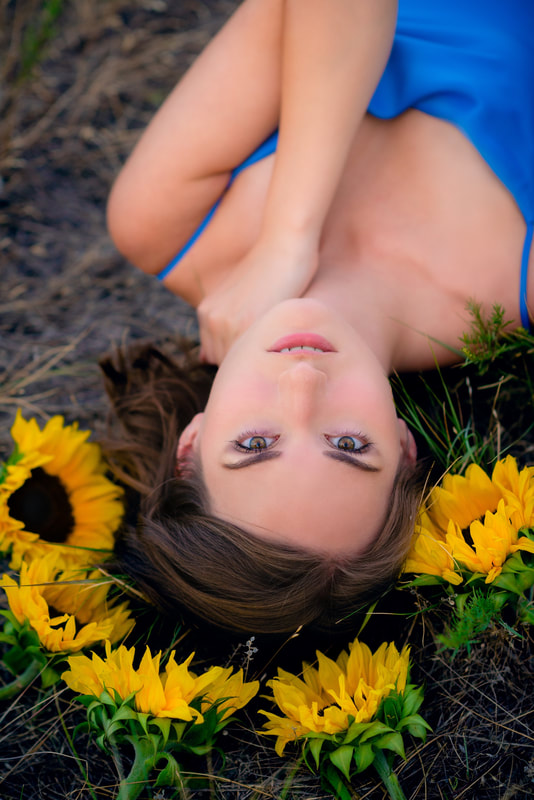 Girl laying in field with yellow sunflowers for senior pictures