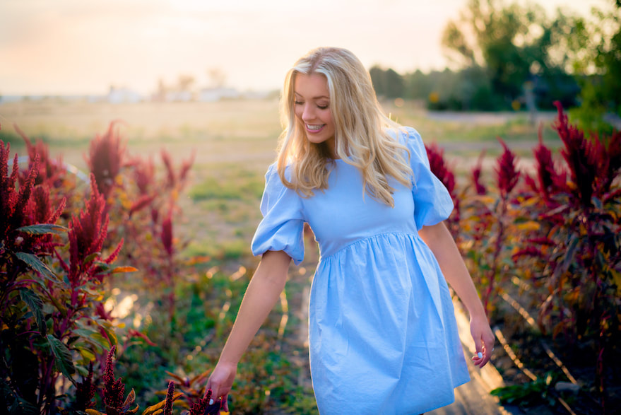 Blonde girl in blue dress smiling down at flowers for senior pictures