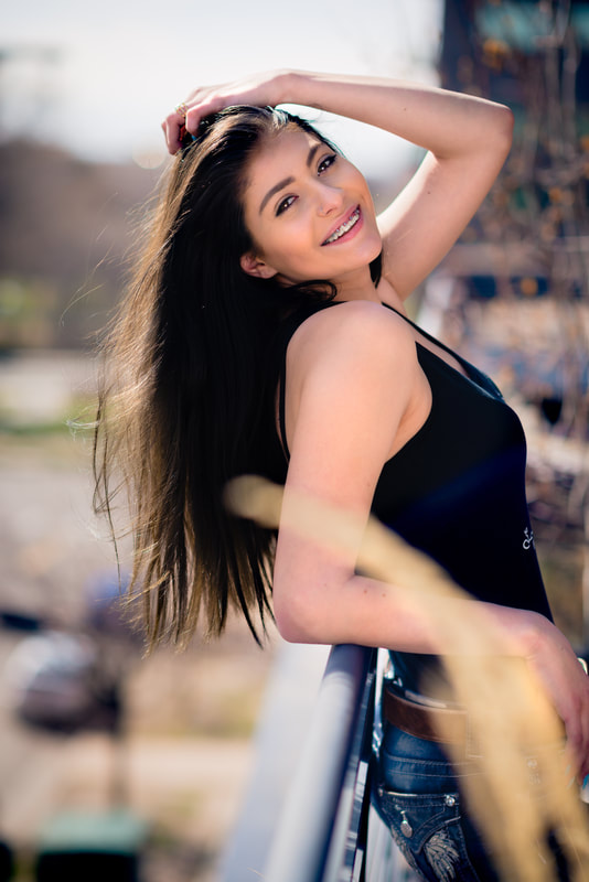 girl with brown hair leaning backwards over railing with hand in hair smiling for senior pictures