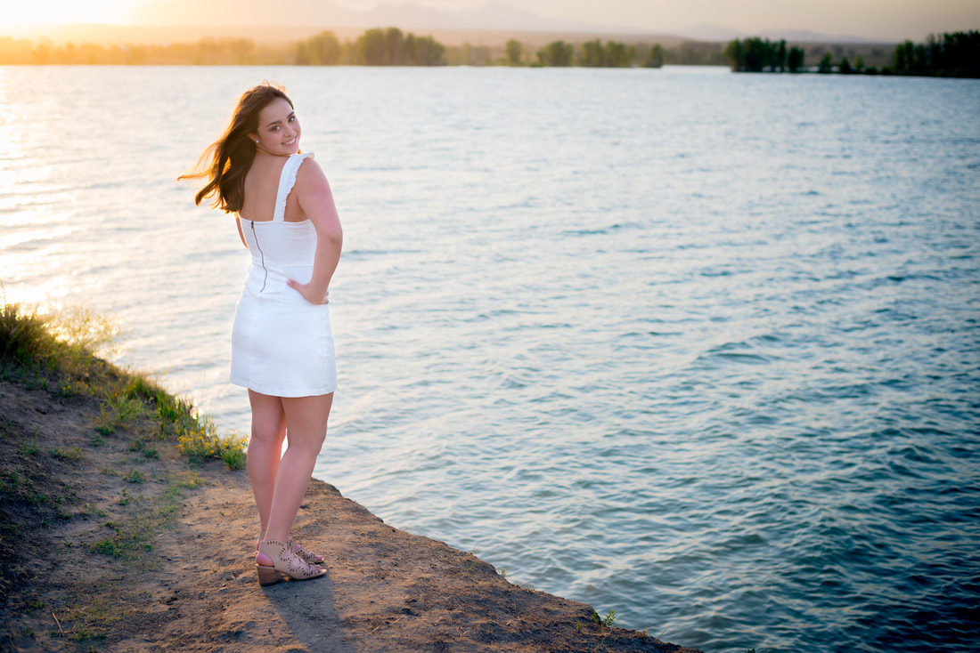 Girl in white dress standing by lake for senior pictures