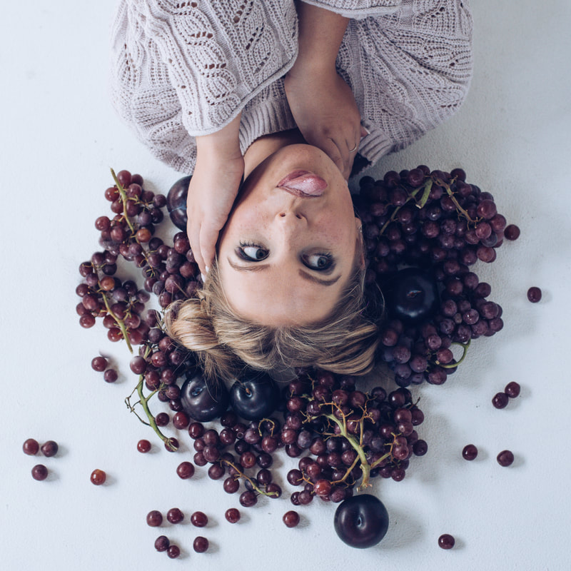 girl laying on ground with tongue sticking out surrounded by grapes and plums for senior pictures
