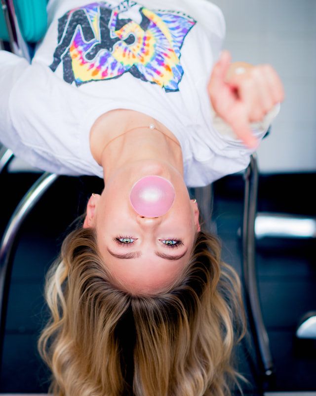 girl hanging upside down pointing at camera blowing bubble gum for senior pictures