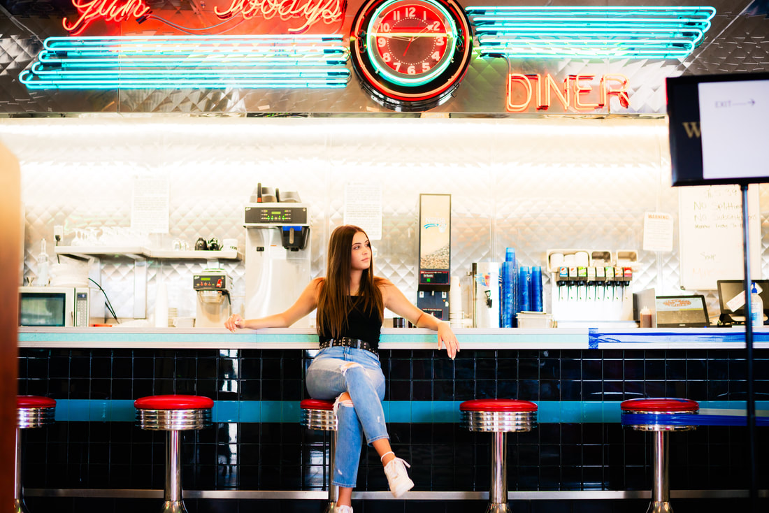 Girl sitting at 1950s themed diner with red bar stools for senior pictures
